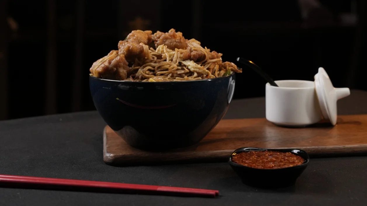 Chilli garlic noodles in a dark bowl with chopsticks and chilli sauce, shot for a Hyderabad restaurant's social media