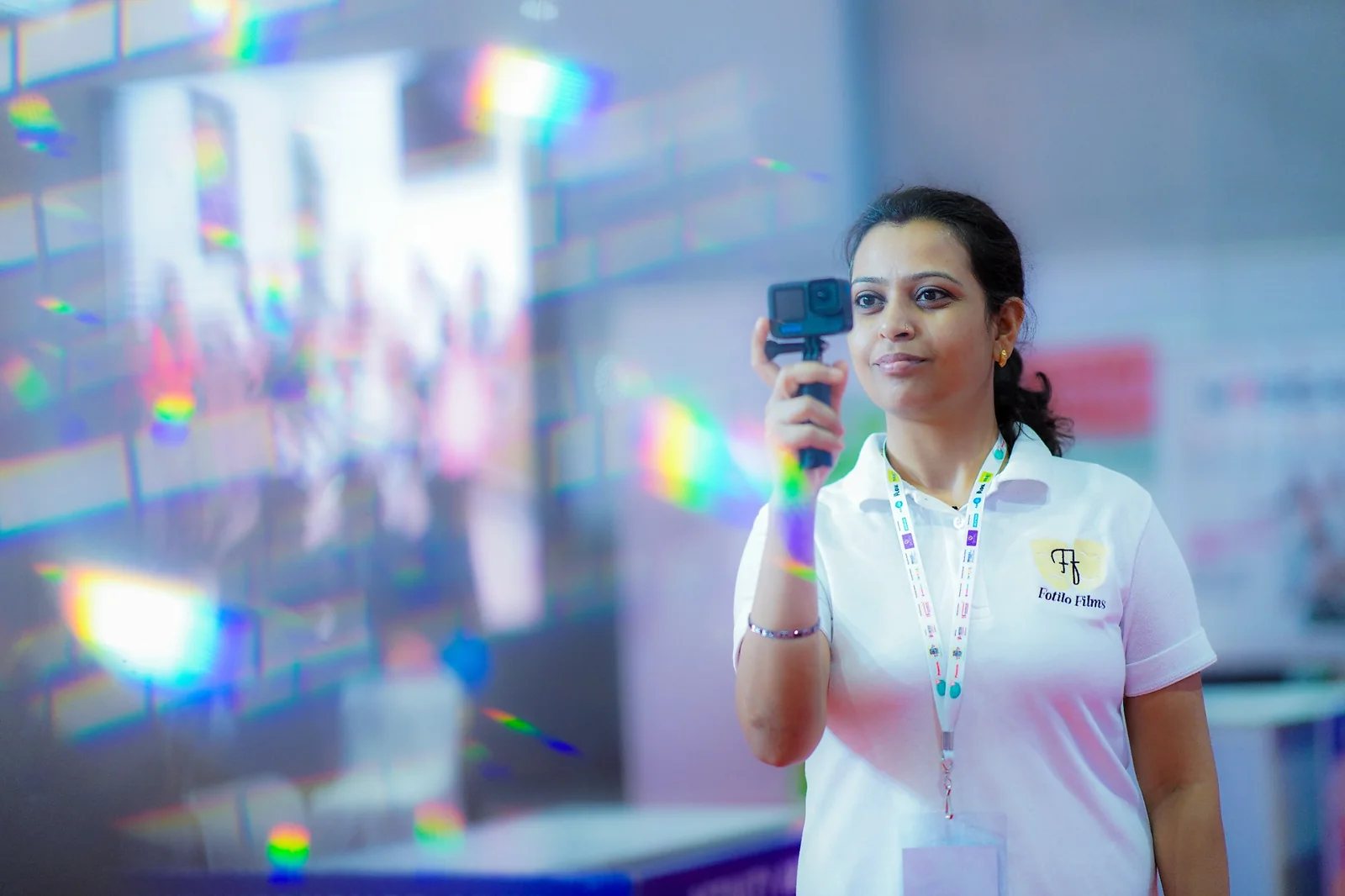 Vipasha Kiran holding an action camera during a shoot, with colourful reflections in the foreground.